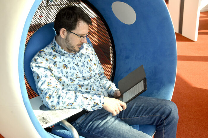 Ein Mann sitzt in einem Sonic-Chair und liest in einem Ebook-Reader.
