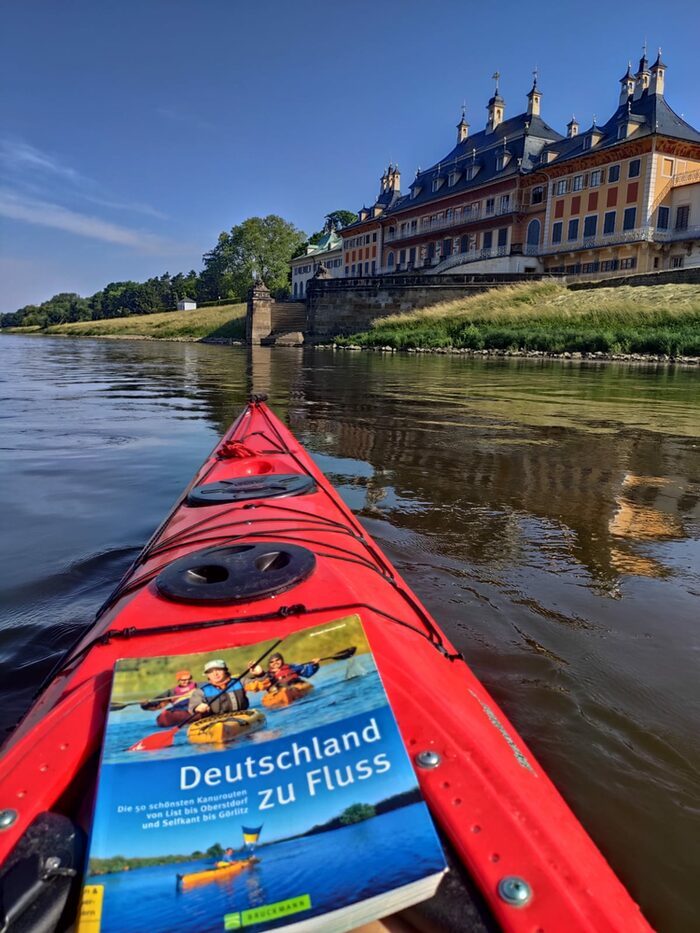 Auf dem Foto sieht man ein Kajak mit einem Buch im Vordergrund und einem Schloss im Hintergrund.