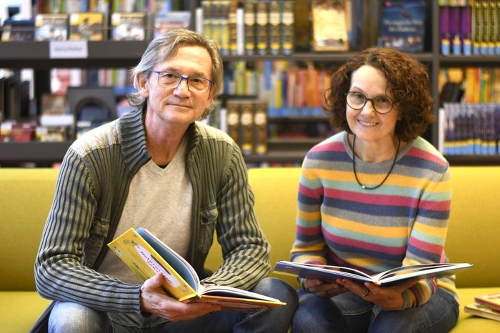 Eine Frau und ein Mann sitzen mit aufgeschlagenen Kinderbüchern in einer Bibliothek.