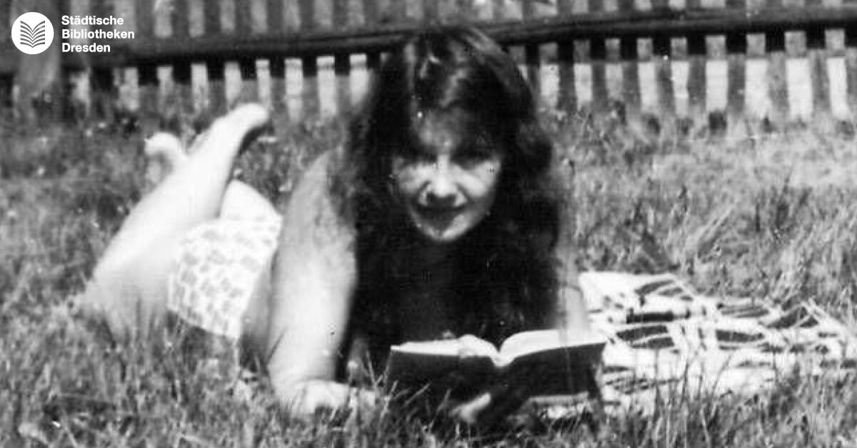 Schwarz-weiß Bild einer jungen Frau, die auf einer Decke im Gras liegt und liest.