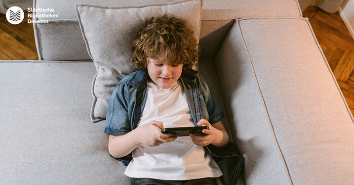 Ein Kind liegt auf einem Sofa und spielt auf einem Smartphone.