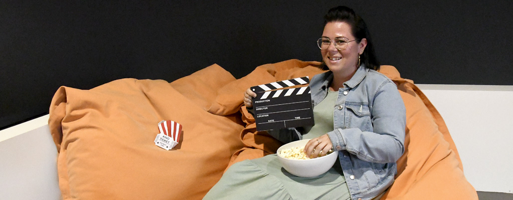 Frau mit Popcorn sitz auf gemütlichen Kissen und wird Film schauen