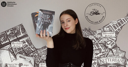 Eine Person zeigt die beiden Bücher der Krähen-Duologie, im Hintergrund ist die Karte der fiktiven Stadt Ketterdam zu sehen
