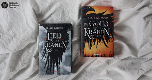 Die beiden Bücher "Das Lied der Krähen" und "Das Gold der Krähen" liegen auf einem hellen Hintergrund