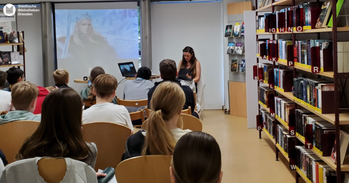 Frau mit Publikum vor einer Leinwand